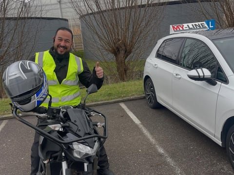 Geslaagde motorrijder in een geel hesje met helm bij de lesmotor