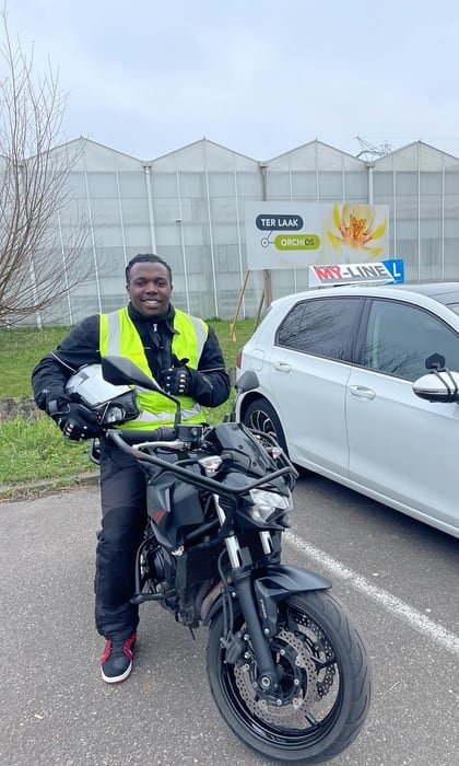 Geslaagde motorrijder in een geel hesje bij de lesmotor en de lesauto